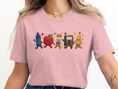 Pink t-shirt features cartoon crayon, apple, pencil, and notebook characters dancing.