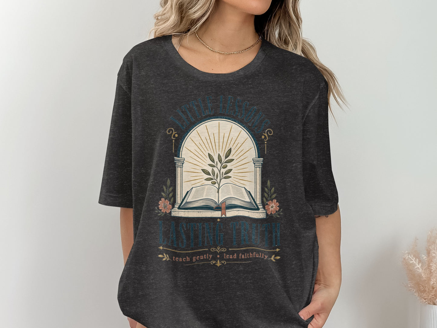 Dark grey t-shirt with "Little Lessons, Lasting Truth" graphic of open book and branch.