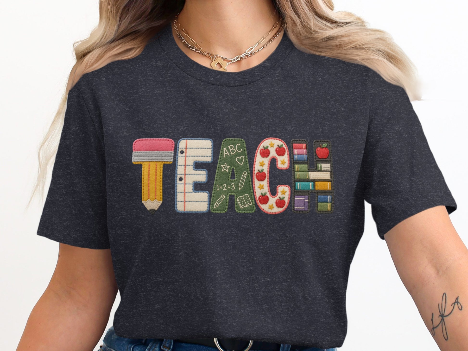 Dark t-shirt with embroidered TEACH lettering featuring school-themed icons.