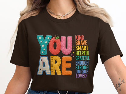 "You Are" text with uplifting words, on a brown t-shirt.