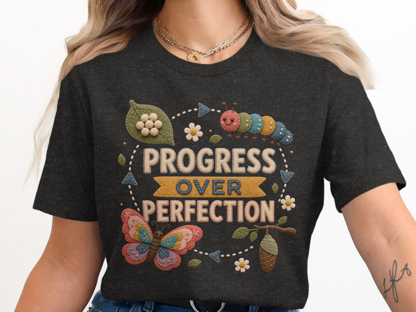 Dark t-shirt with embroidered "Progress Over Perfection" text, butterfly, caterpillar, and chrysalis.