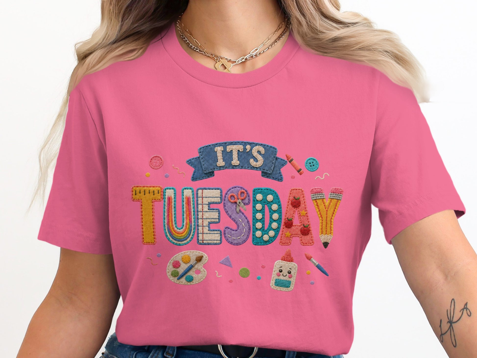 Pink t-shirt with embroidered "IT'S TUESDAY" text and art supplies.