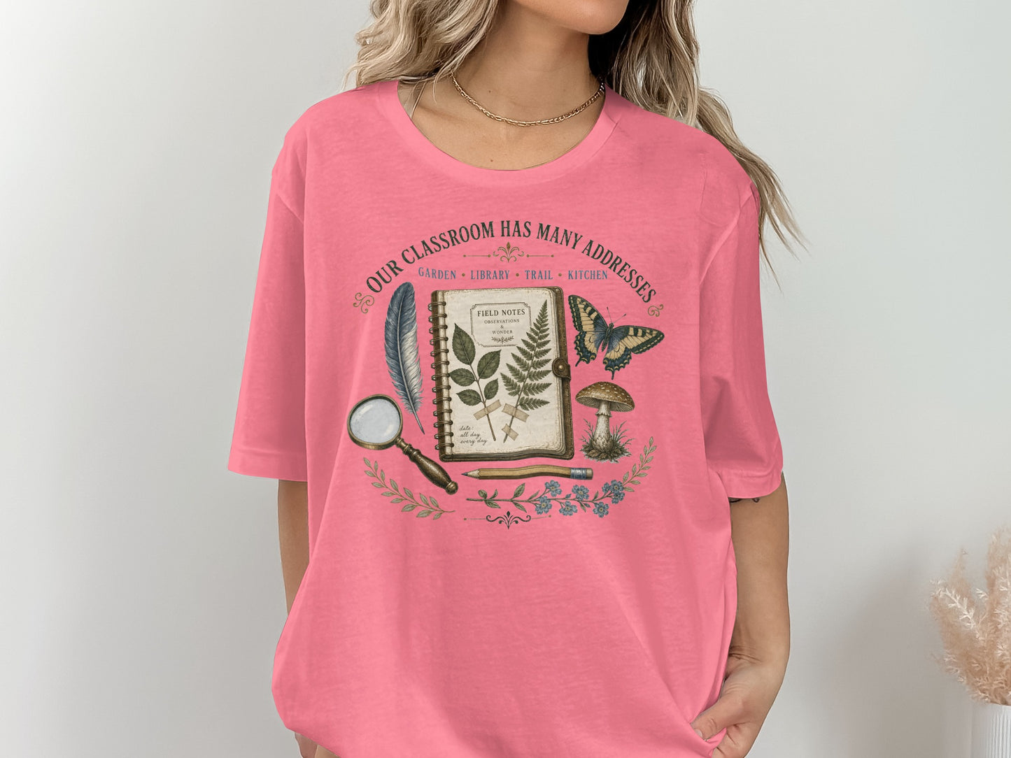 T-shirt graphic: "Our Classroom Has Many Addresses" with field journal, feather, butterfly, and mushroom.
