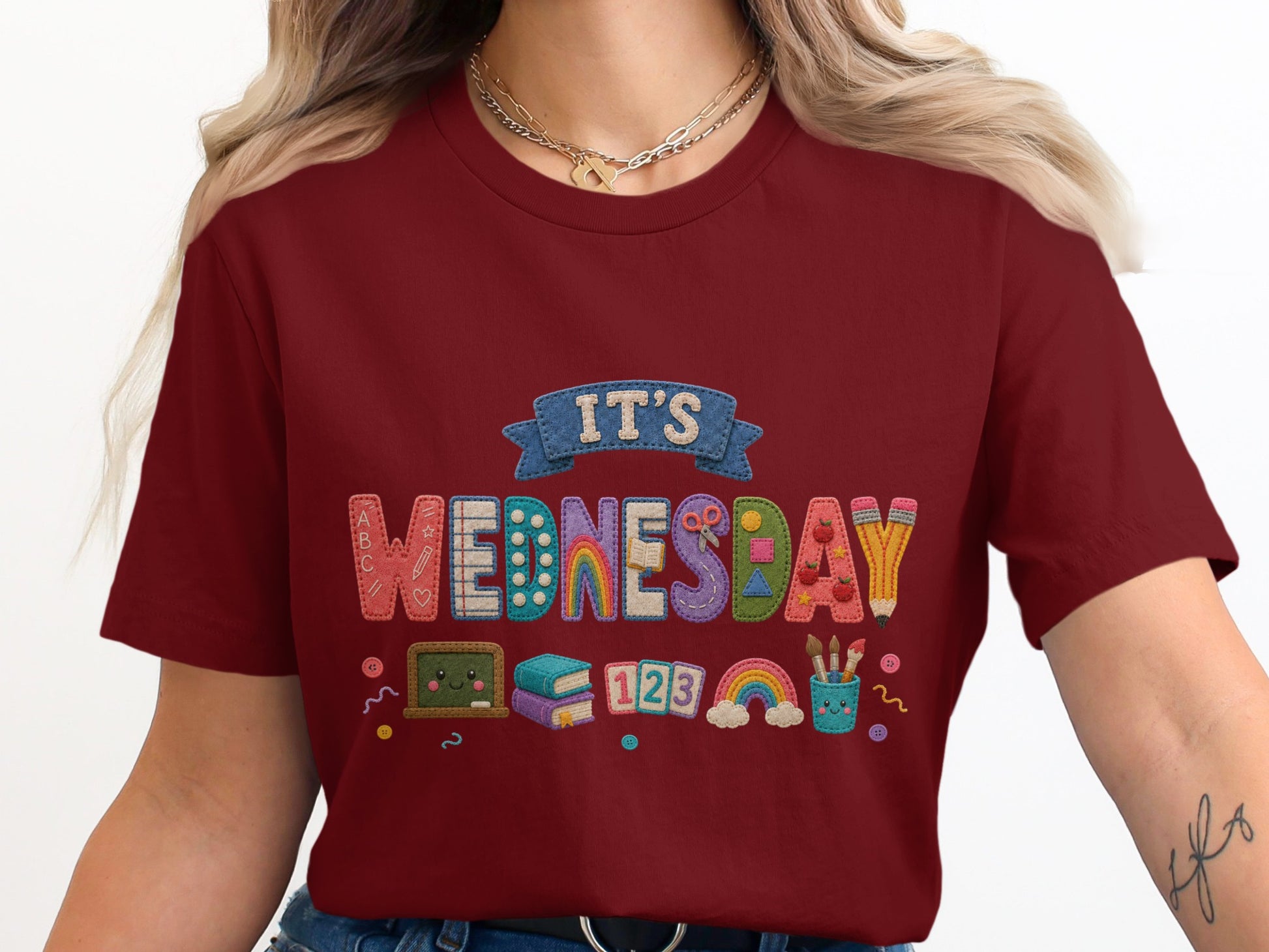 Maroon shirt with colorful embroidered "IT'S WEDNESDAY" text featuring school supplies and icons.