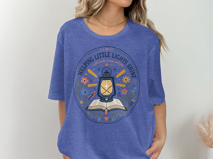 Blue t-shirt with "Helping Little Lights Shine" text and lantern on open book design.