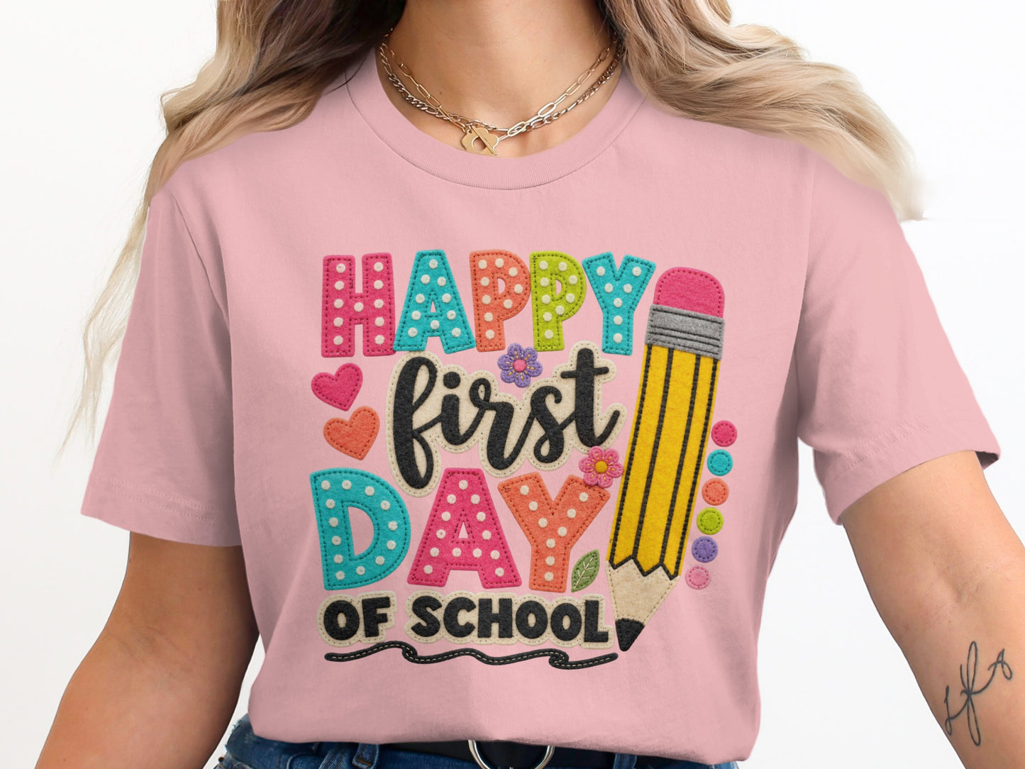 Pink t-shirt with colorful "Happy first day of school" text and pencil design.