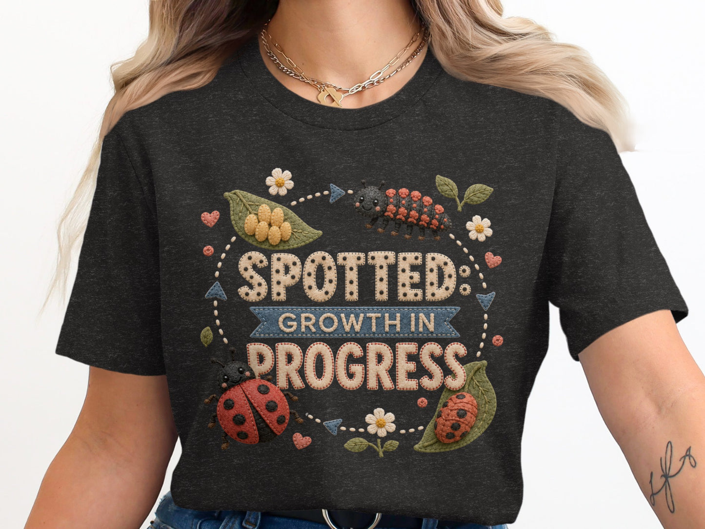 Spotted: Growth in Progress text with ladybugs, caterpillar, and flowers on a dark shirt.