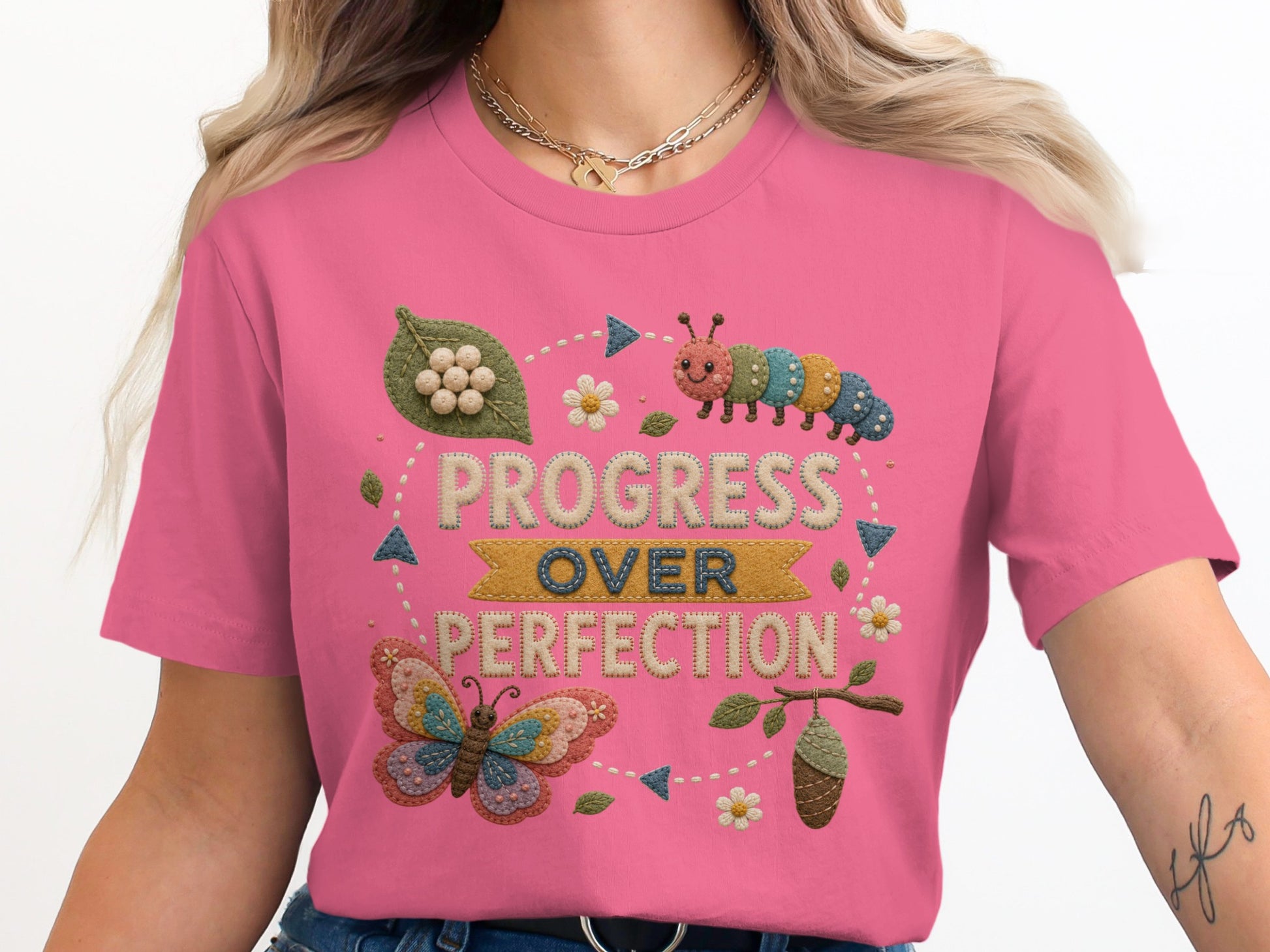 Pink t-shirt with embroidered caterpillar, butterfly, and the text "PROGRESS OVER PERFECTION".
