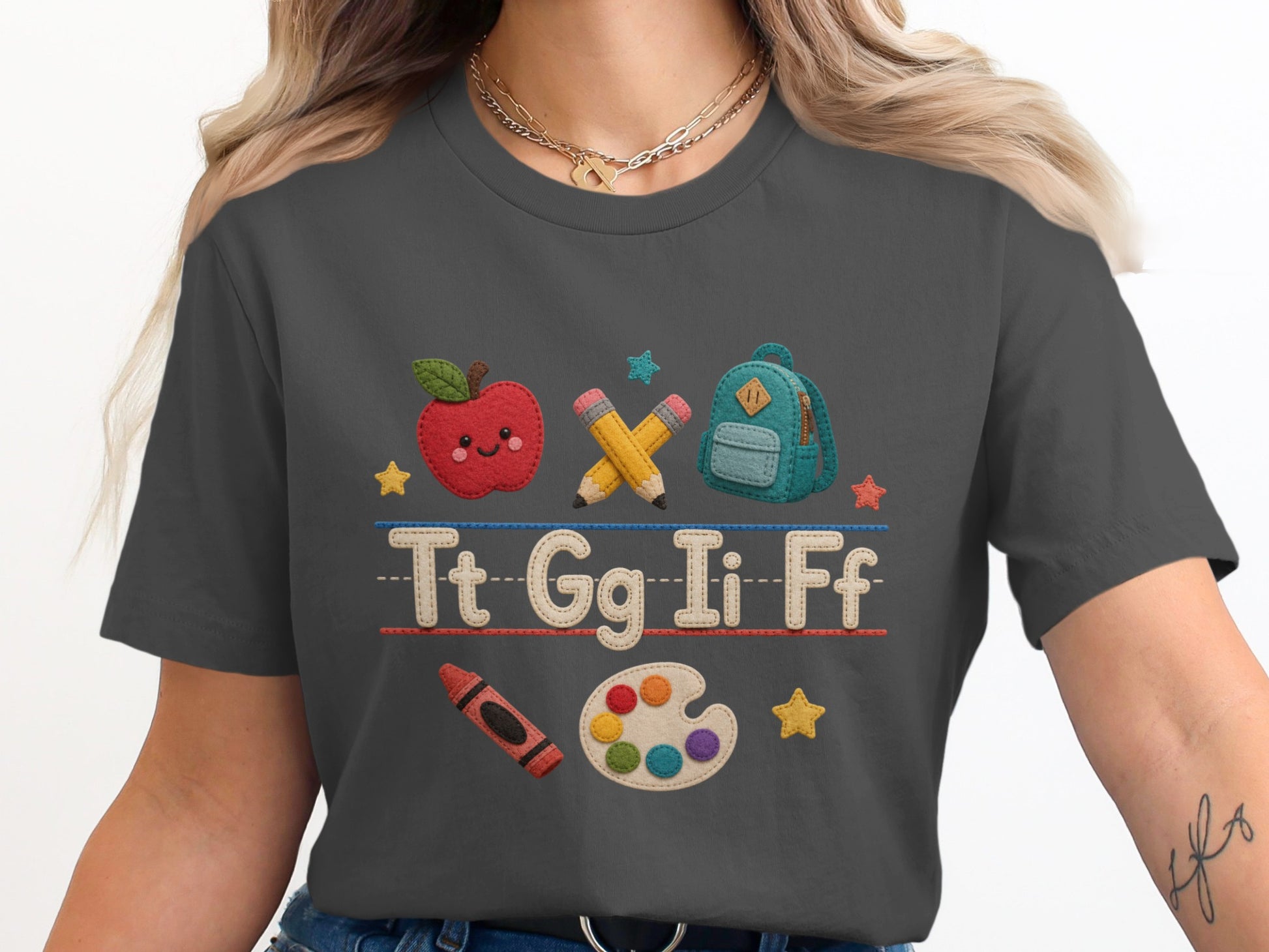 Graphic tee with apple, backpack, pencils, letters, crayon, and paint palette.