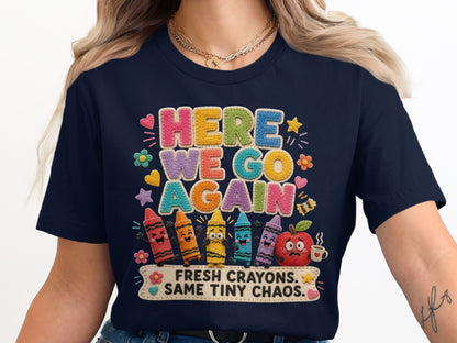 Navy t-shirt with colorful "HERE WE GO AGAIN" text, smiling crayons, and apple.