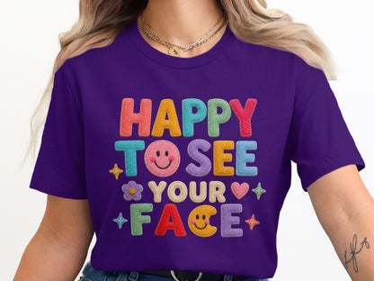 Purple t-shirt with "HAPPY TO SEE YOUR FACE" embroidered in colorful letters and icons.