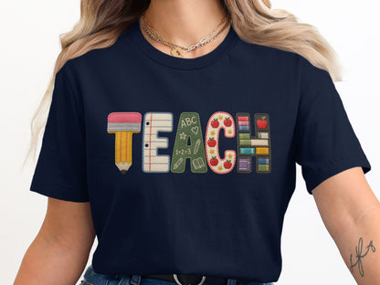 Navy t-shirt with embroidered "TEACH" design featuring pencil, notebook, chalkboards, apples, and books.