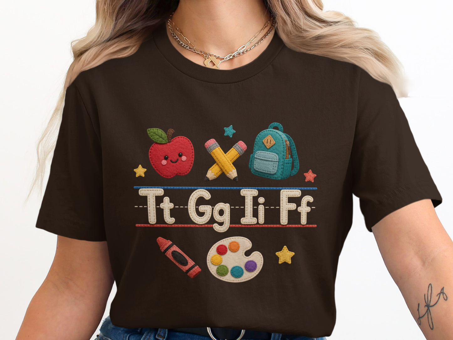 Brown t-shirt with embroidered cartoon apple, pencils, backpack, letters, crayon, and paint palette.