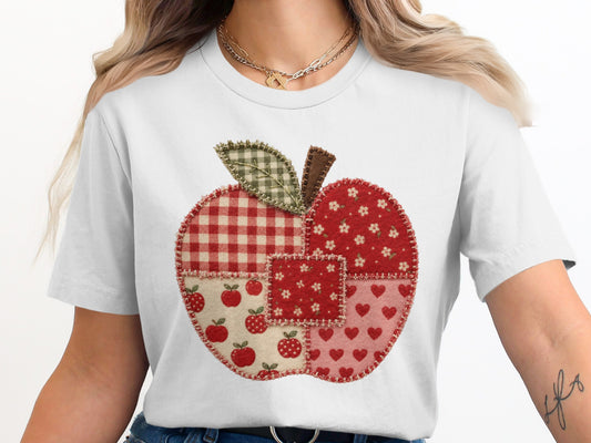 White t-shirt with a red patchwork apple design featuring plaid, apples, and hearts.