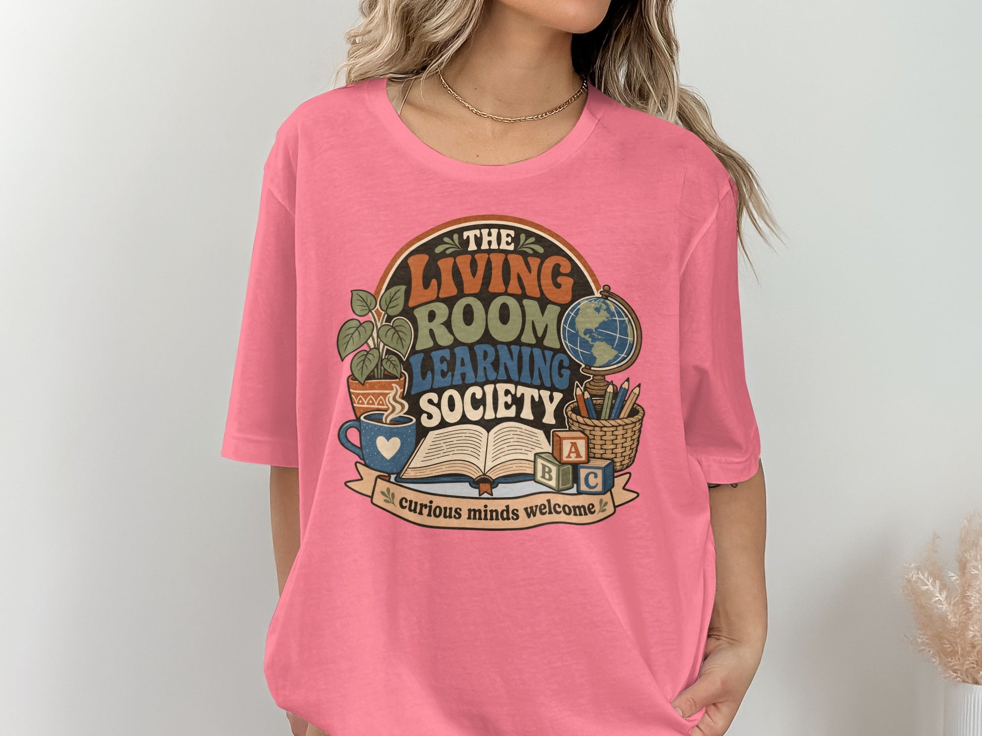 Pink t-shirt with "The Living Room Learning Society" retro graphic and "curious minds welcome" text.