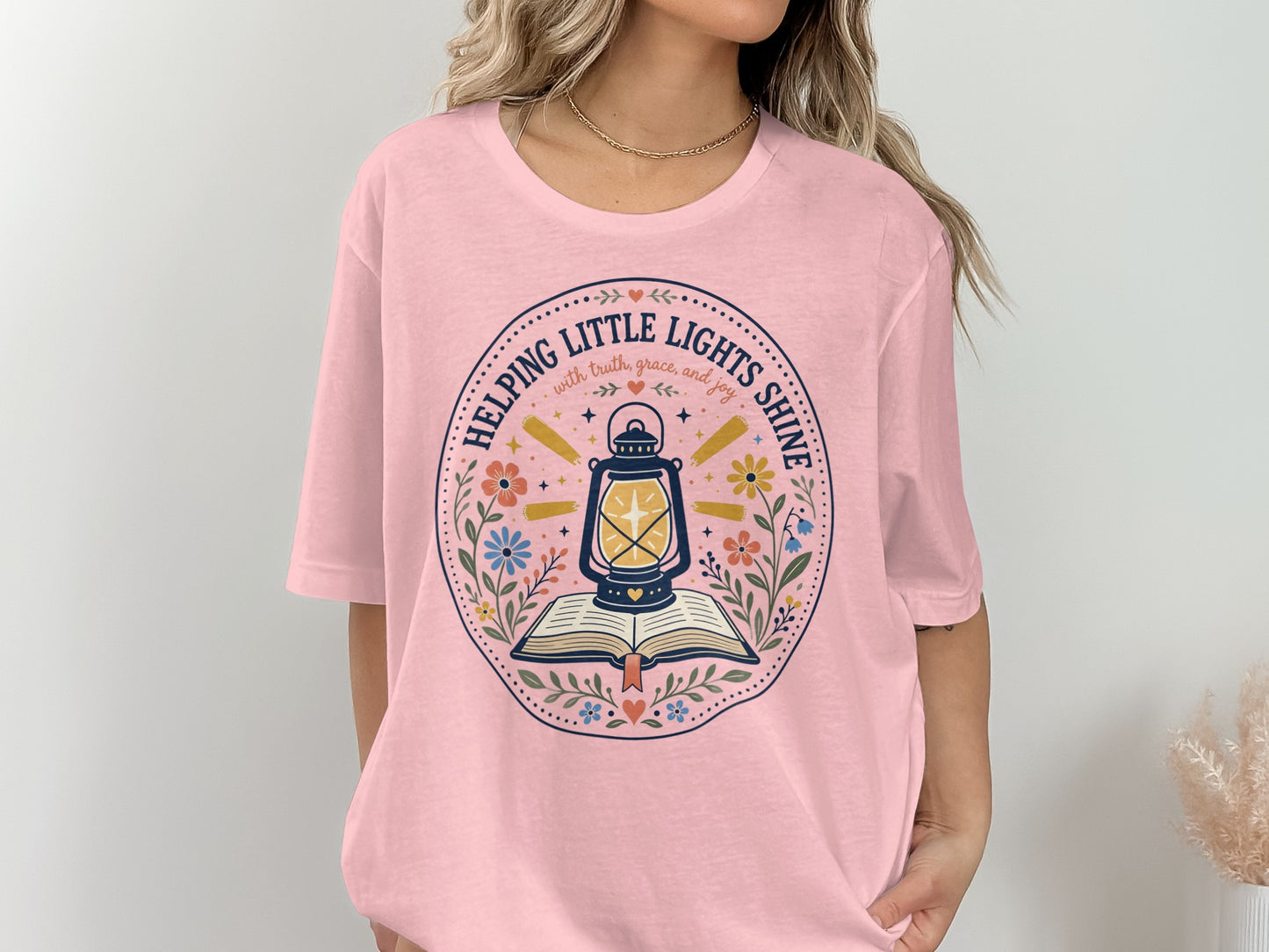 Pink t-shirt with a circular design of a lantern above an open book.