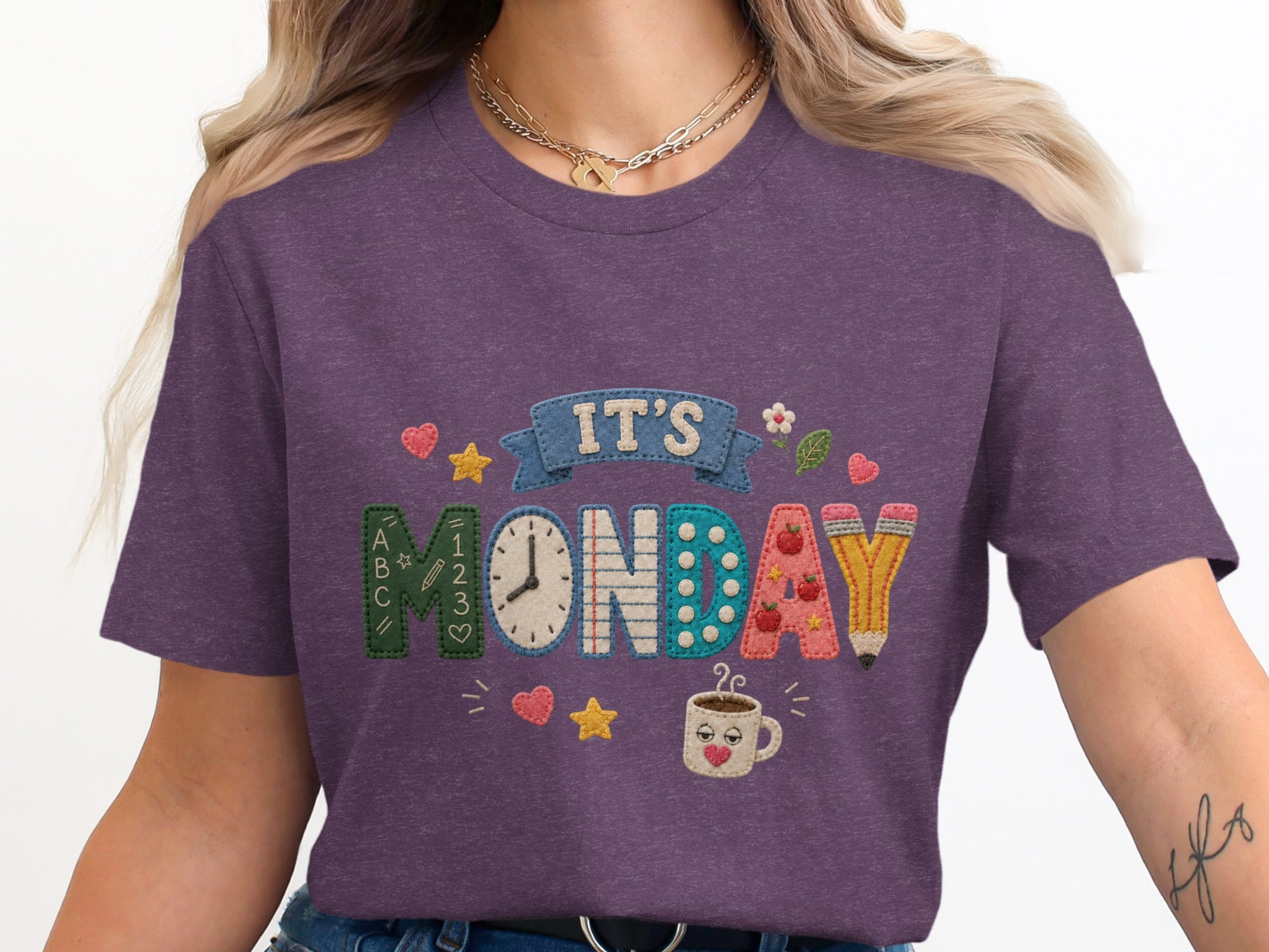 Purple t-shirt with embroidered text "IT'S MONDAY" and school-themed graphics.