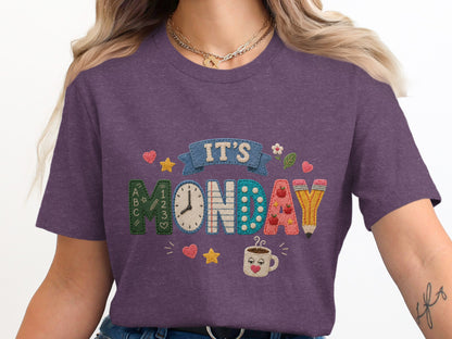 Purple t-shirt with embroidered text "IT'S MONDAY" and school-themed graphics.