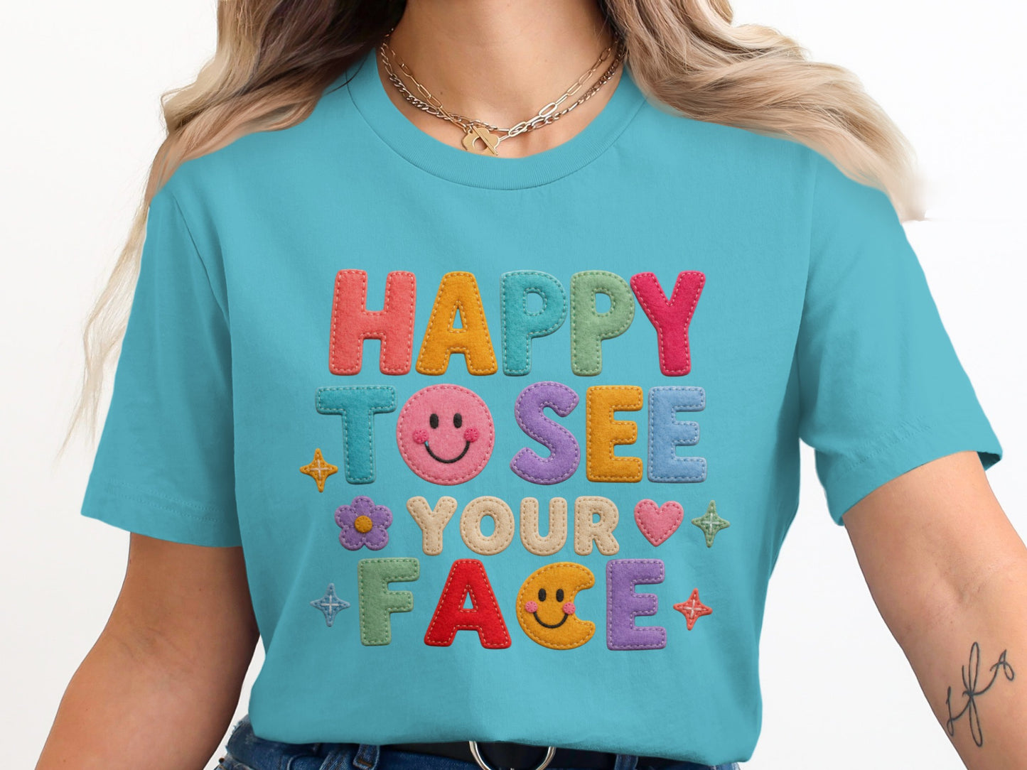 Teal t-shirt with embroidered letters reading "HAPPY TO SEE YOUR FACE."