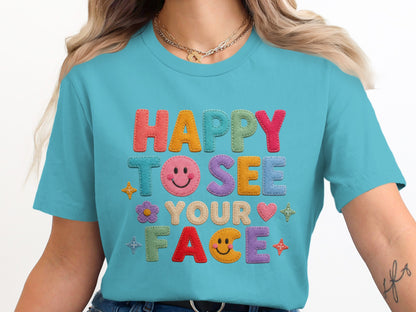 Teal t-shirt with embroidered letters reading "HAPPY TO SEE YOUR FACE."