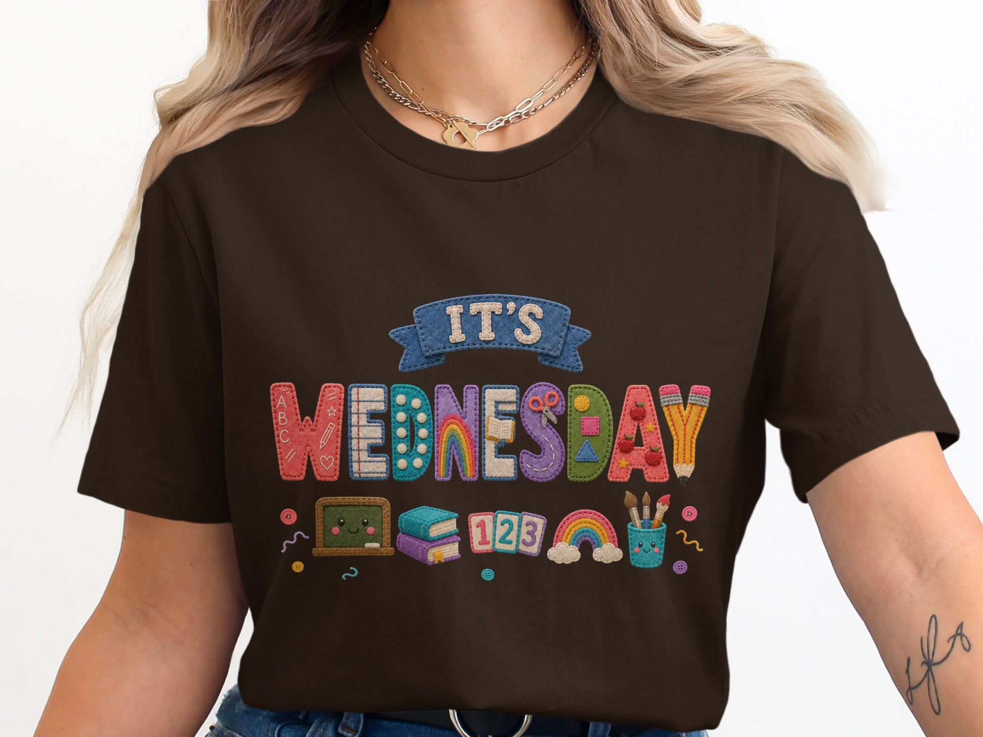 Brown t-shirt with "IT'S WEDNESDAY" displayed with school-themed embroidered letters and graphics.