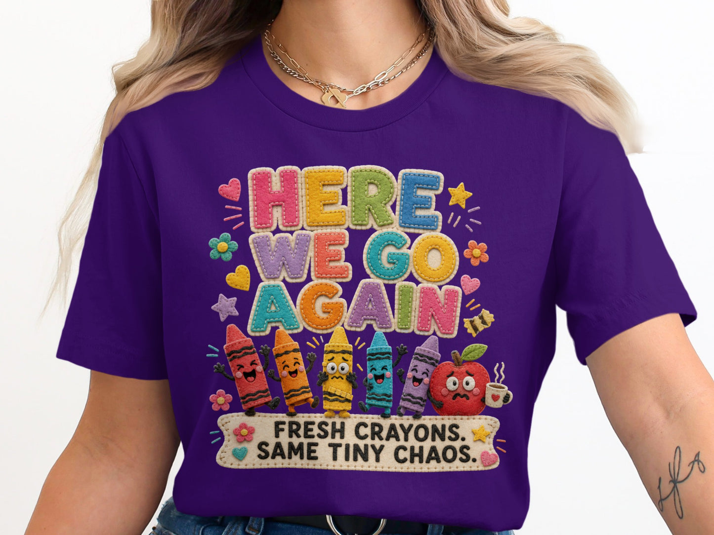 Purple t-shirt with "HERE WE GO AGAIN" text and art of crayons and an apple.