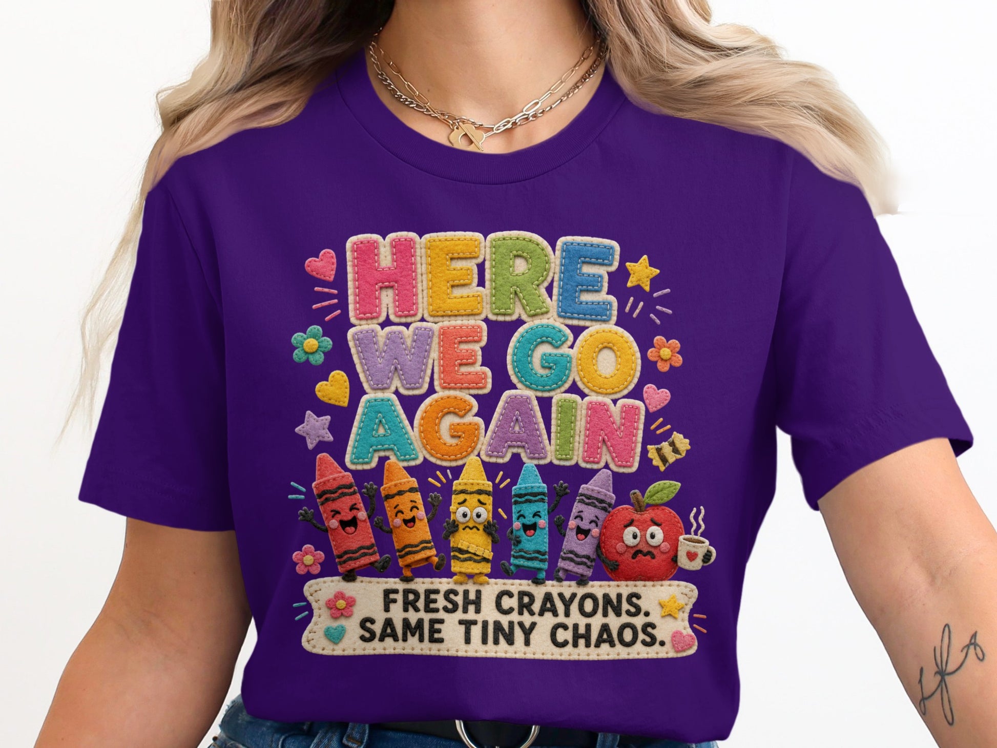Purple t-shirt with "HERE WE GO AGAIN" text and art of crayons and an apple.