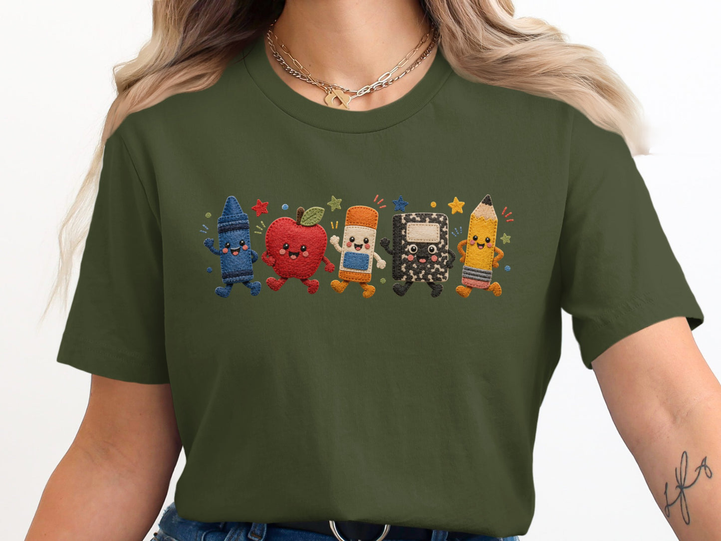 Olive green t-shirt with embroidered smiling crayon, apple, eraser, notebook, and pencil characters.