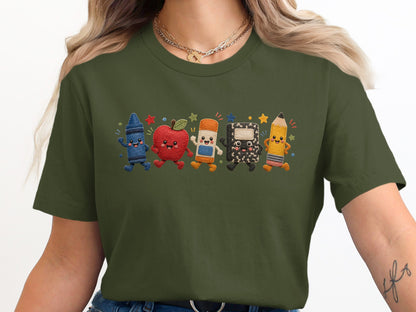 Olive green t-shirt with embroidered smiling crayon, apple, eraser, notebook, and pencil characters.