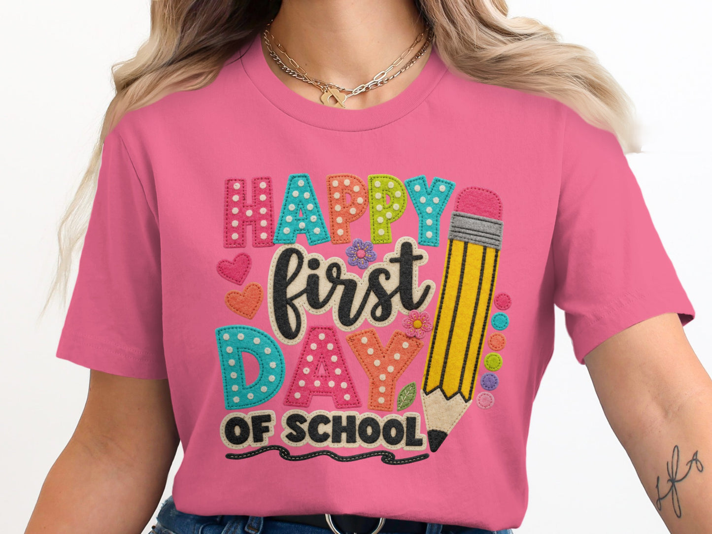 Happy First Day Of School text with pencil and heart graphics on a pink shirt.