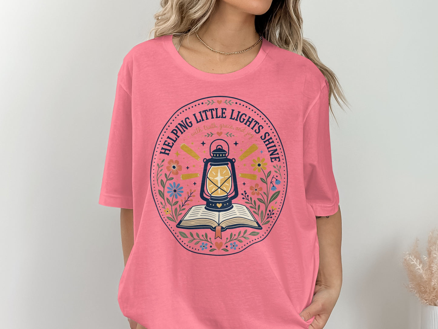 Pink t-shirt with a circular design featuring a lamp over a book and text.