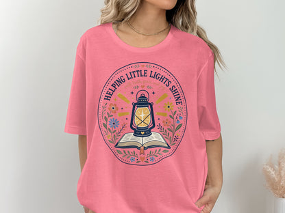 Pink t-shirt with a circular design featuring a lamp over a book and text.