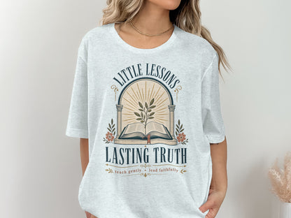 Light grey t-shirt with "Little Lessons Lasting Truth" graphic of an open book and plant.