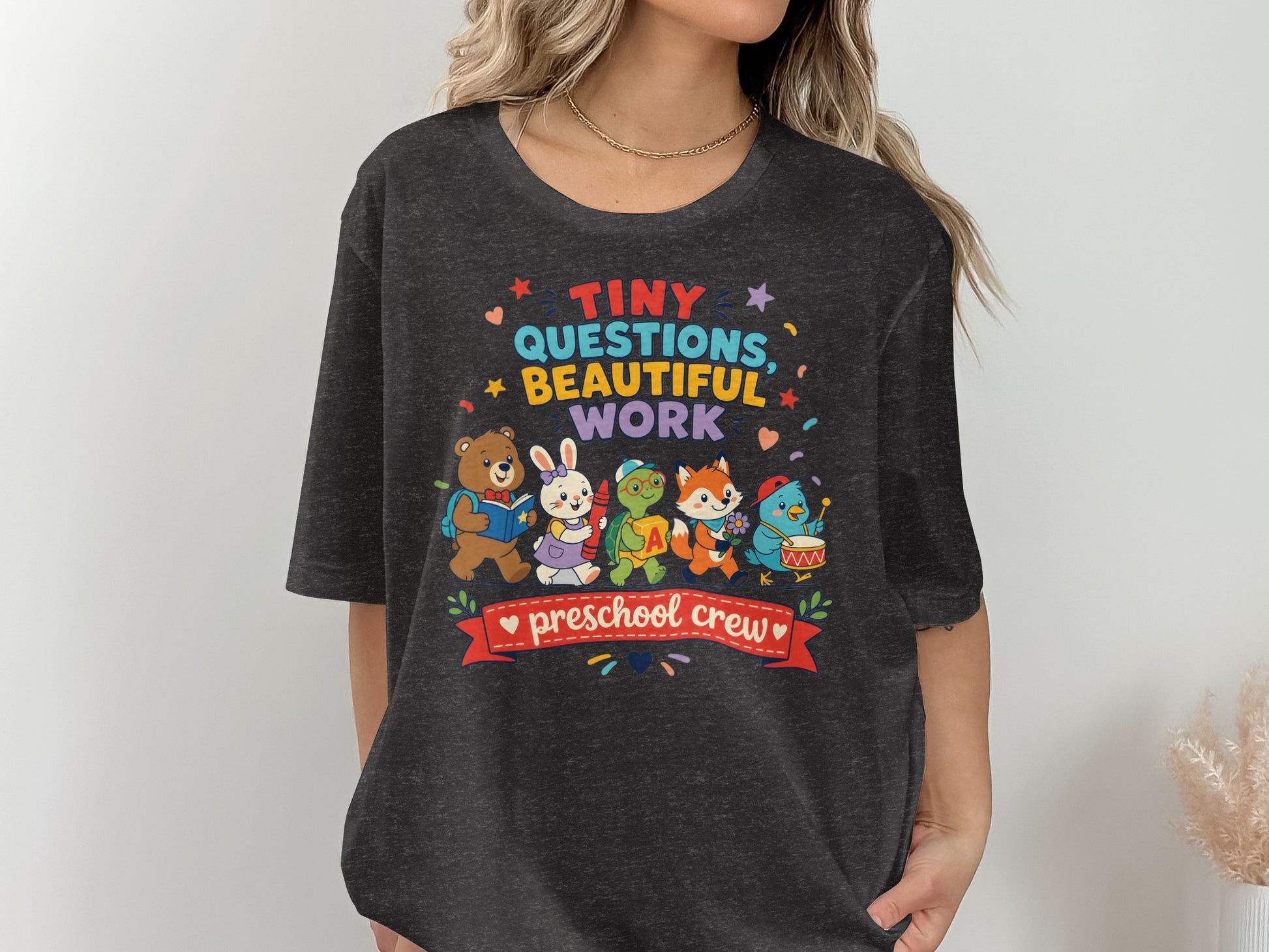 Dark t-shirt with cartoon animals and text "Tiny Questions, Beautiful Work Preschool Crew".