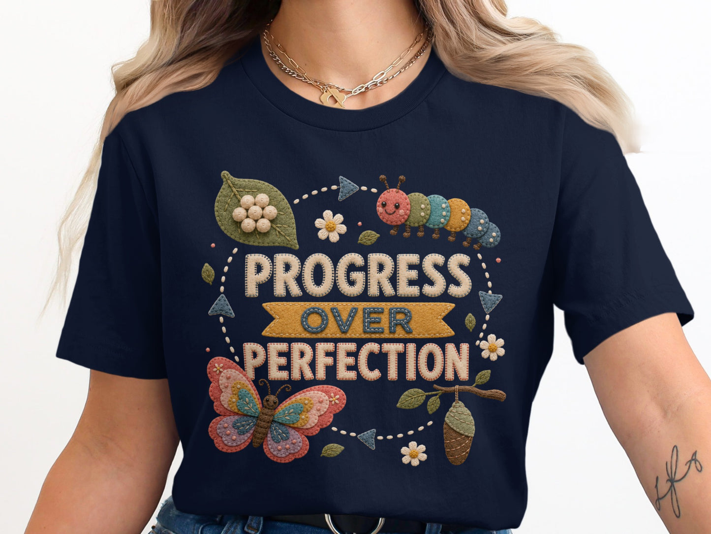 Navy t-shirt with embroidered text "PROGRESS OVER PERFECTION" and butterfly imagery.
