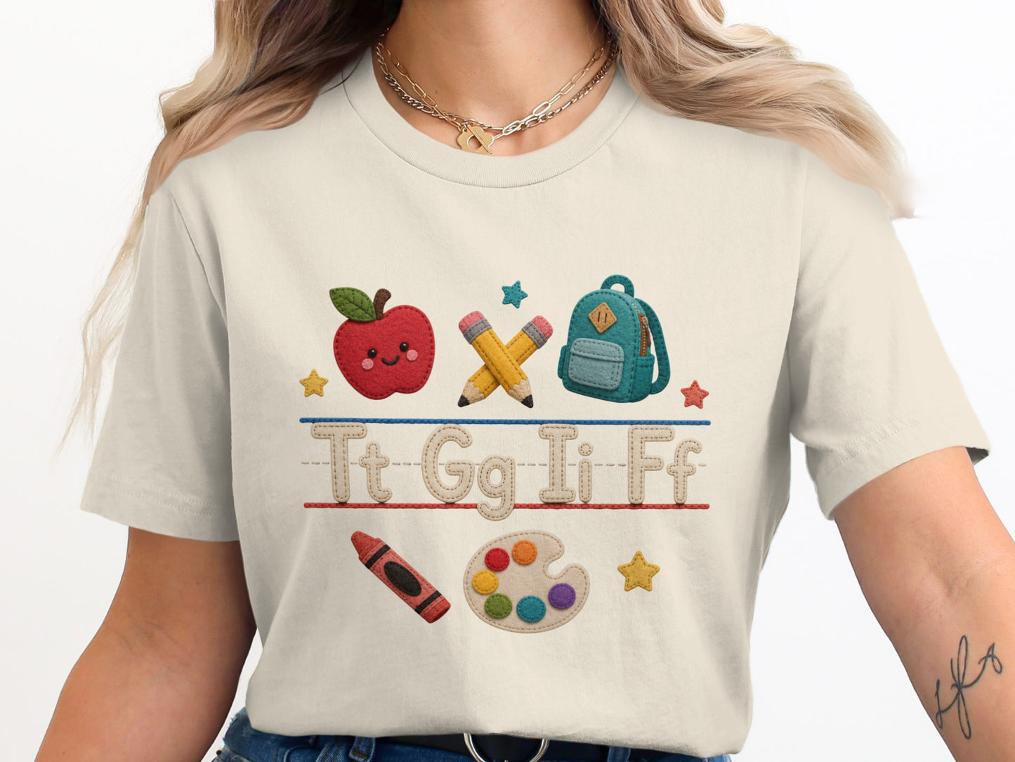 T-shirt with embroidered school graphics: apple, pencils, backpack, crayon, paint palette, stars, and letters.