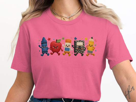 Pink t-shirt with embroidered cartoon school supplies: crayon, apple, eraser, notebook, and pencil.