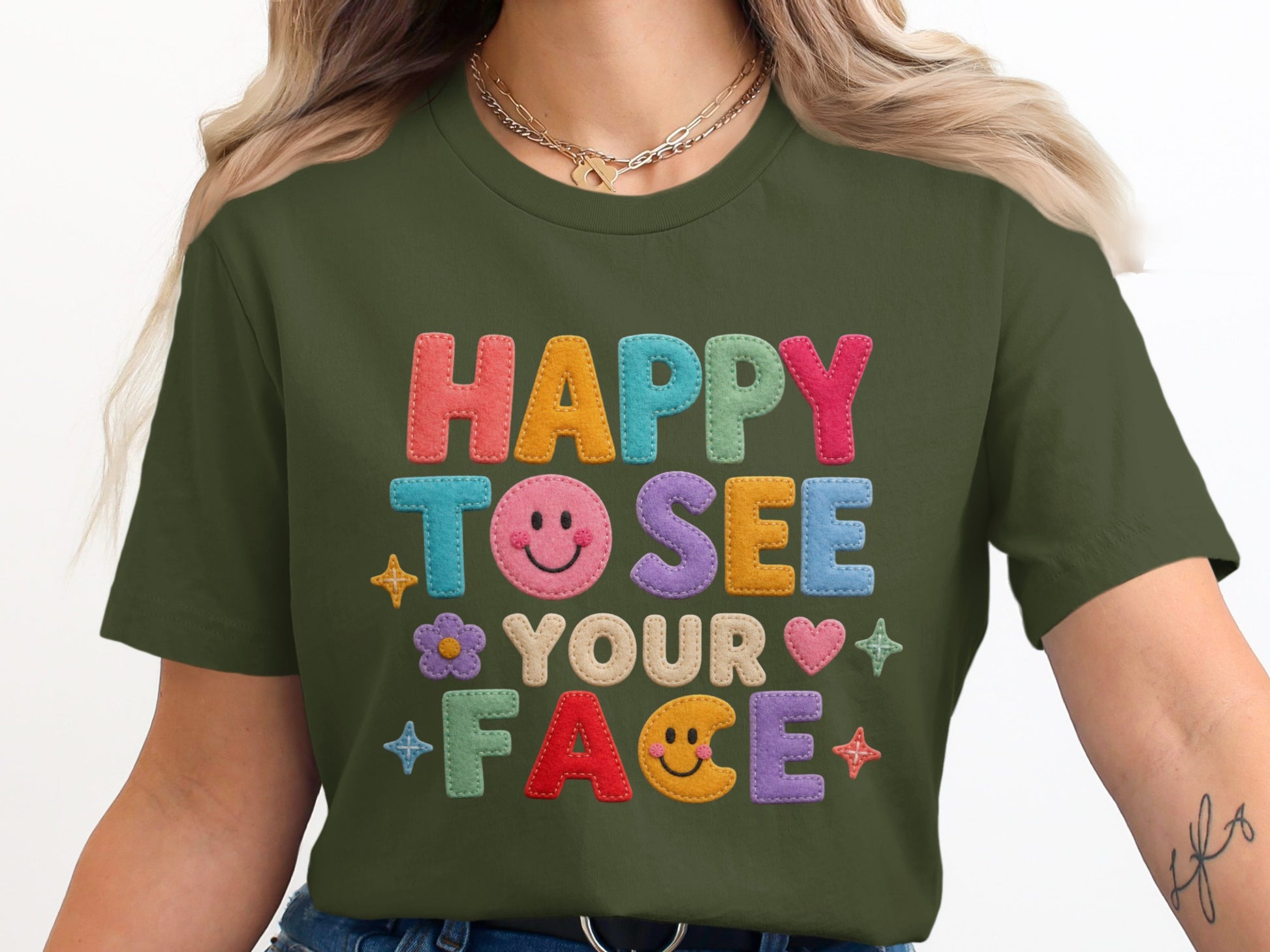 Green t-shirt with "HAPPY TO SEE YOUR FACE" embroidered in colorful lettering.
