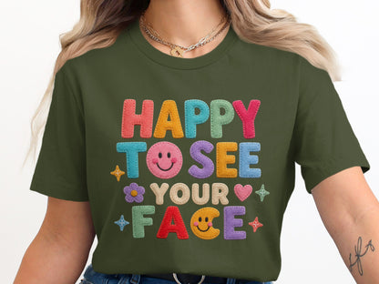 Green t-shirt with "HAPPY TO SEE YOUR FACE" embroidered in colorful lettering.