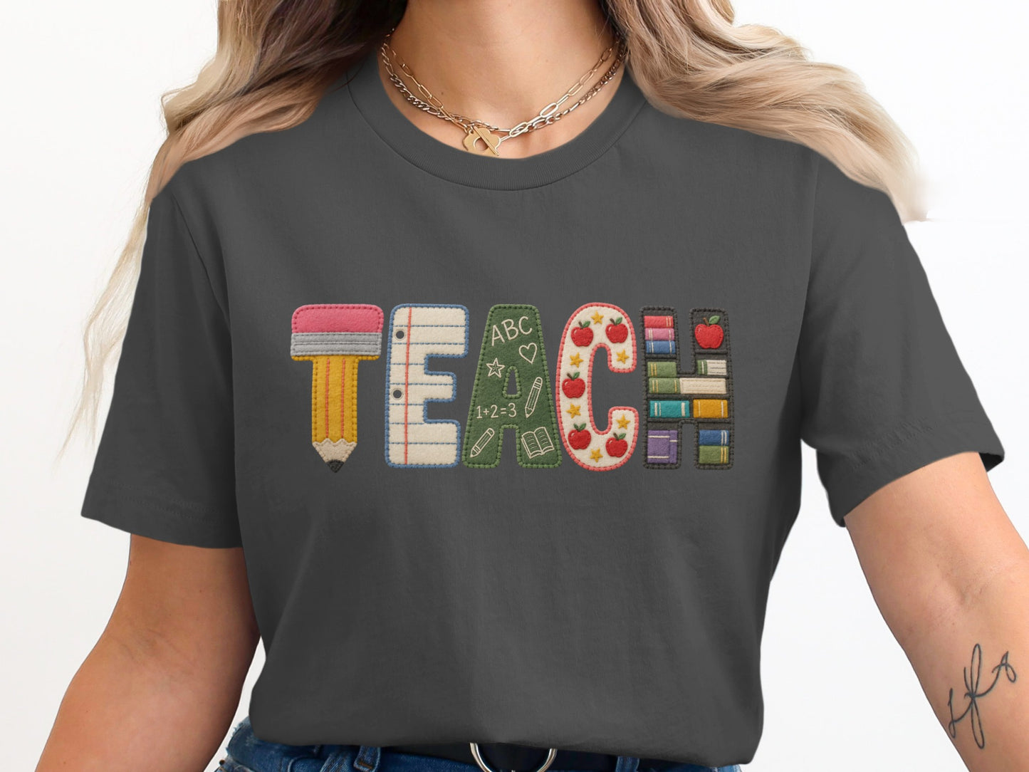 Dark gray t-shirt with "TEACH" embroidered in colorful, educational graphics.