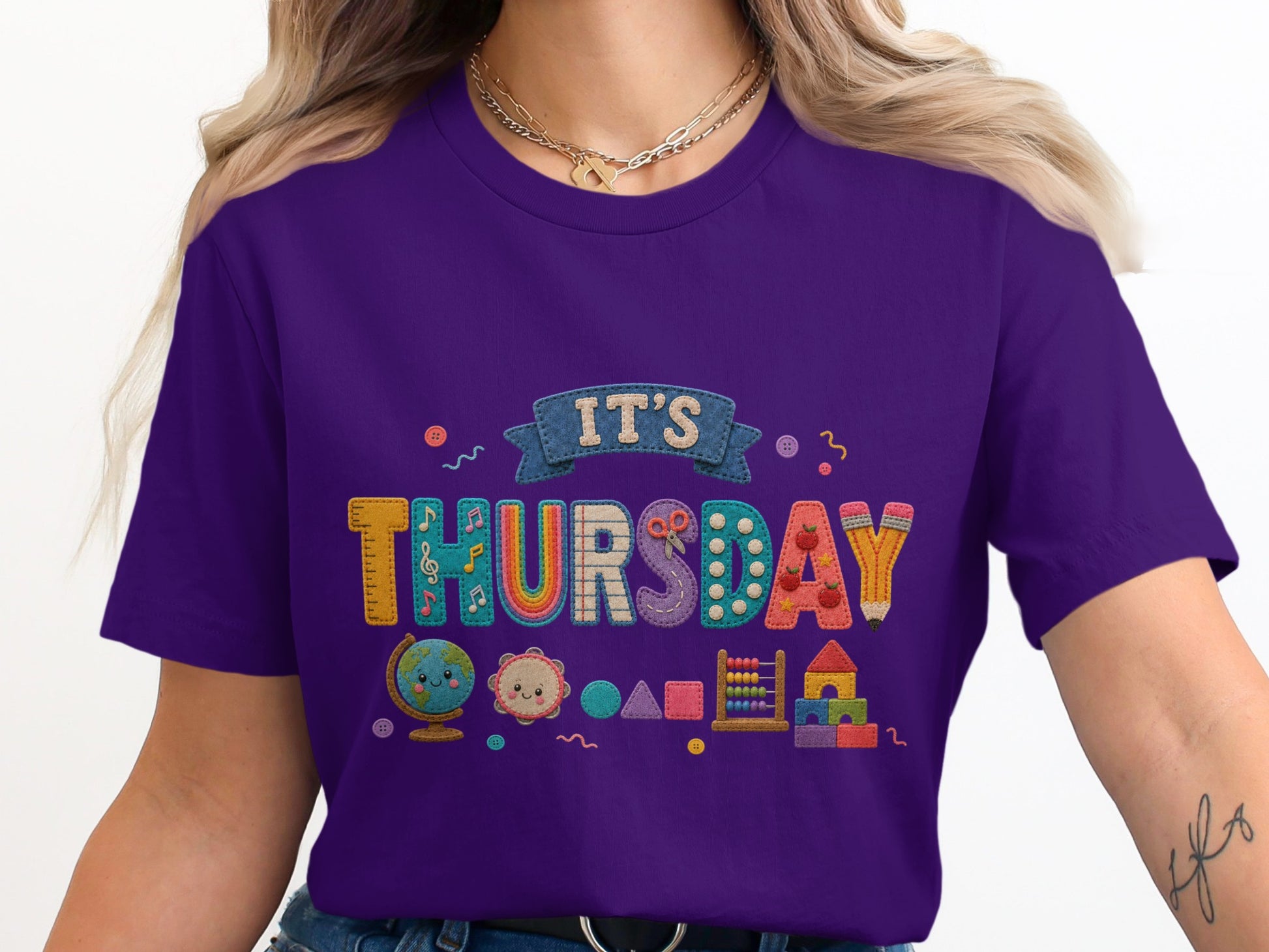Purple t-shirt with multicolor appliquéd letters spelling "IT'S THURSDAY" and school-themed graphics.
