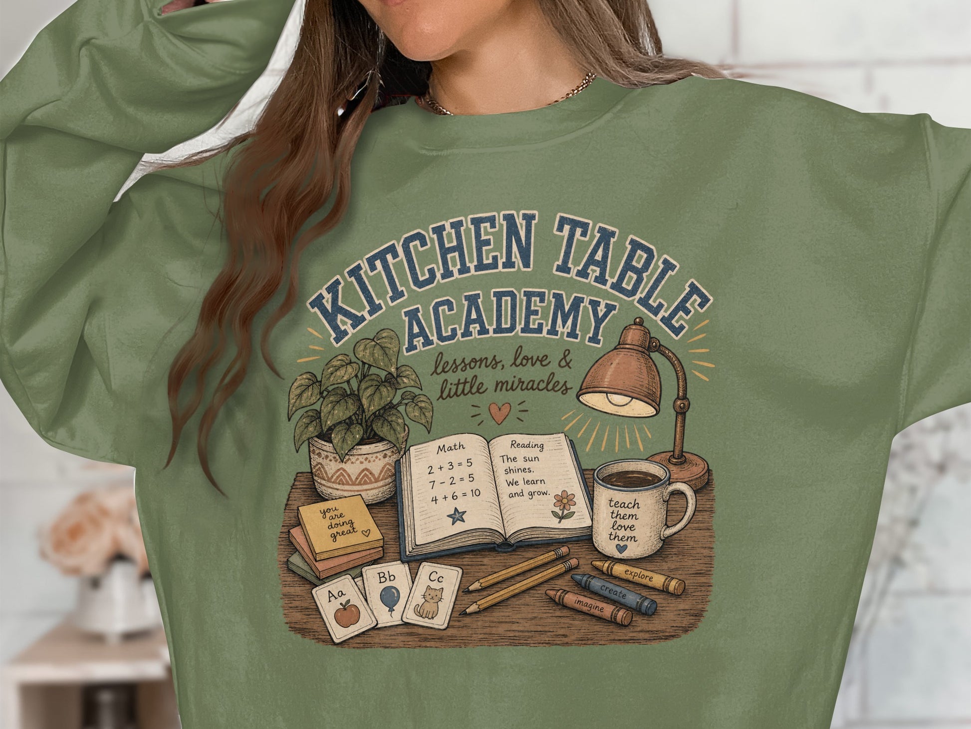 Green sweatshirt with "Kitchen Table Academy" art featuring books, crayons, and alphabet cards.