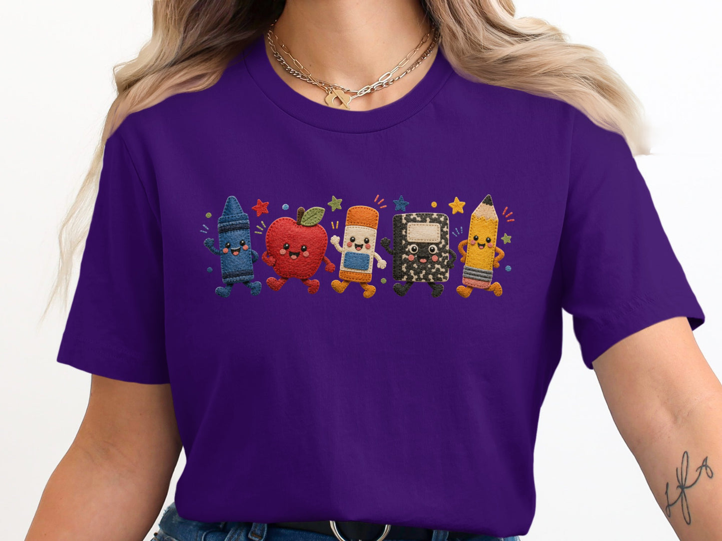 Purple t-shirt with embroidered school supplies characters: crayon, apple, eraser, notebook, and pencil.