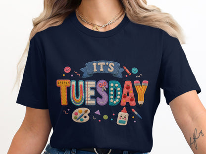 T-shirt with "It's Tuesday" in colorful, textured letters and craft supplies.