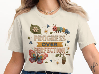 T-shirt with embroidered "Progress Over Perfection" text, caterpillar, butterfly, and chrysalis.
