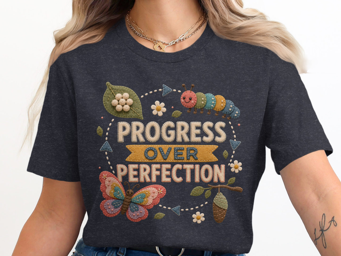 Dark grey t-shirt with "Progress Over Perfection" in embroidered letters, butterfly, caterpillar, and chrysalis.