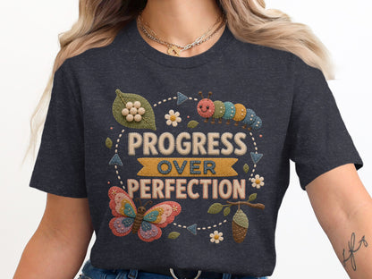 Dark grey t-shirt with "Progress Over Perfection" in embroidered letters, butterfly, caterpillar, and chrysalis.