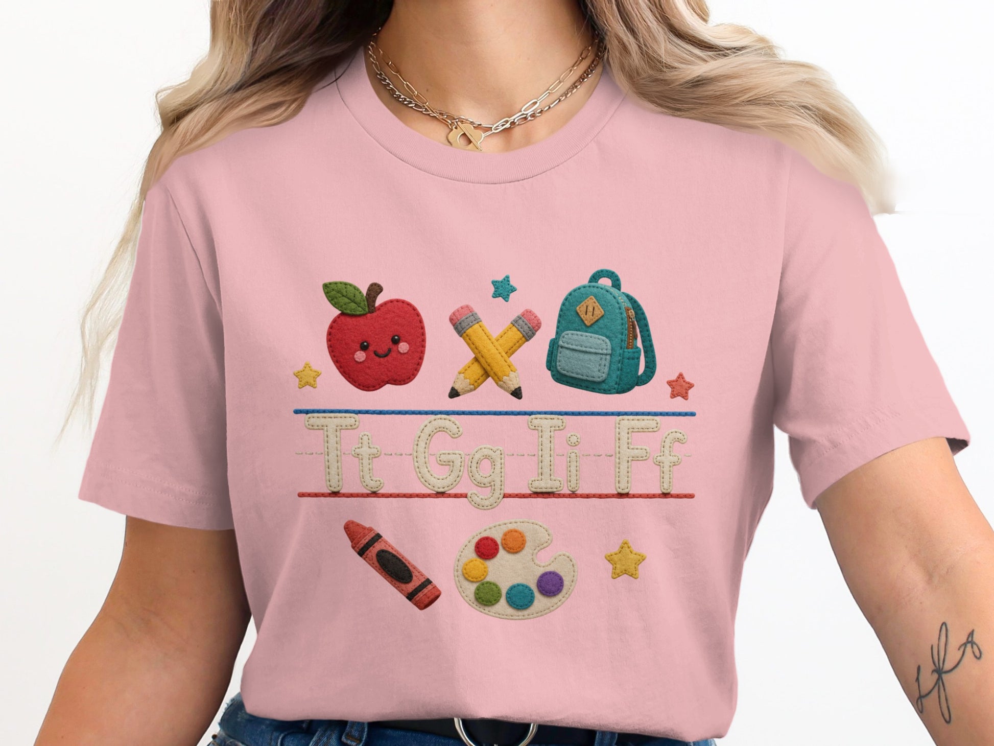 Pink t-shirt with embroidered apple, pencils, backpack, crayon, paint palette, and letters.