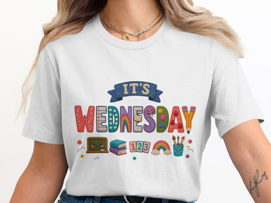 White t-shirt with "IT'S WEDNESDAY" graphic featuring school supplies and rainbows.